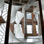 Image: A light, airy, cathedral-like structure installed in a tall industrial space.